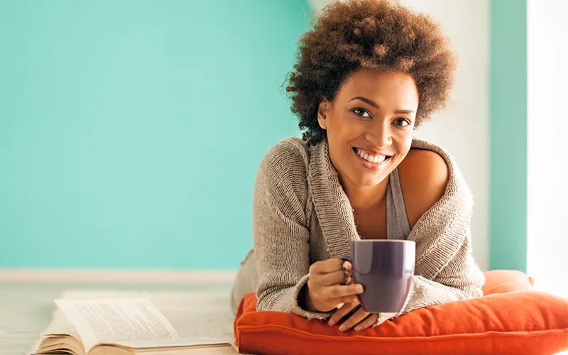 A smiling girl is lying down with a cup in her hands.